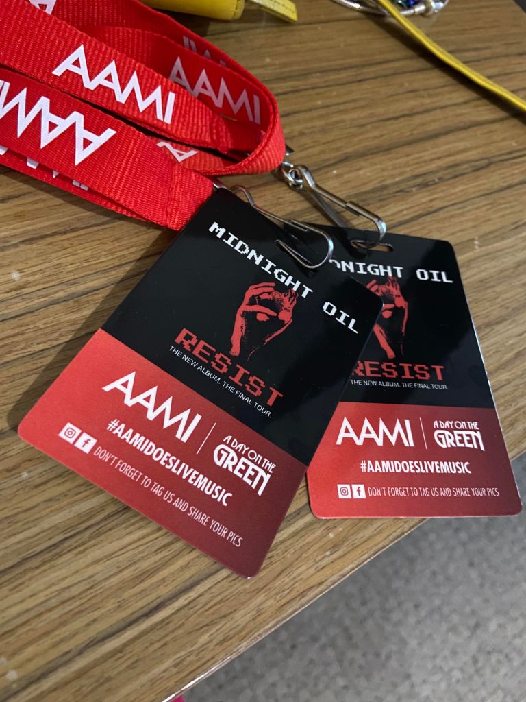 Two Red and Black Tickets, on red AAMI lanyards, with a picture of the Midnight Oil Resist cover - a red first holding a flaming red earth, on a black background. 